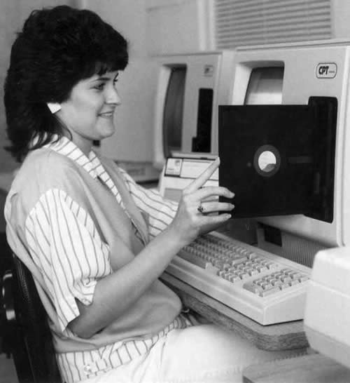 Photo: Woman inserting 8-inch floppy disk into drive of 1970s/1980s-era computer.