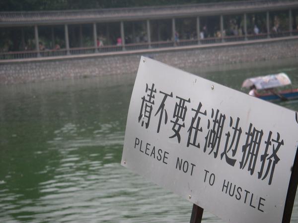 Sign by a river in Chinese and English that reads “PLEASE NOT TO HUSTLE”