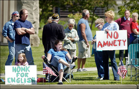 Photo at an anti-immigrant rally. Girl holding up sign saying “Honk for English”; woman holding up sign saying “NO ANMETY”.