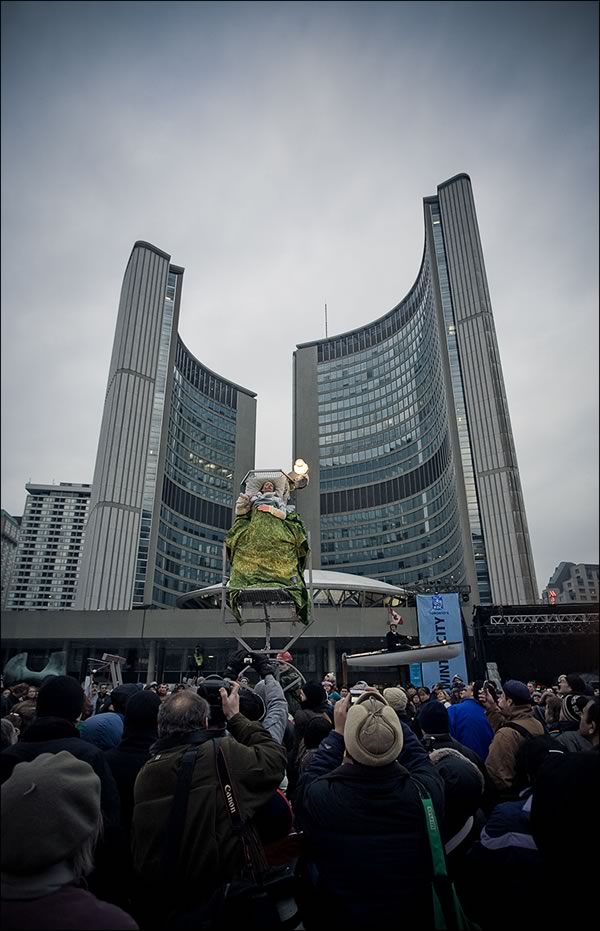 Man in bed suspended in the air with Toronto’s New City Hall in the background