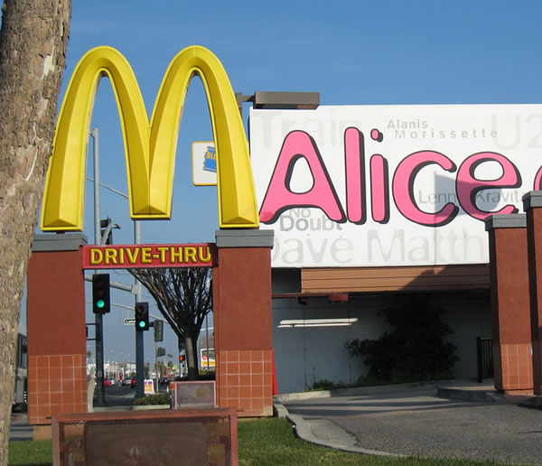 2 signs: McDonald’s “M” in foreground, “Alice” on billboard in background