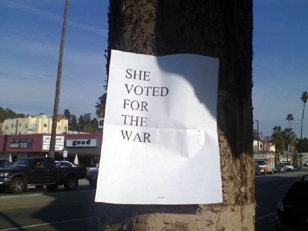 Plain white laser-printed paper stapled to a tree: “SHE VOTED FOR THE WAR”