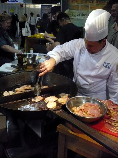 Chef frying peameal bacon in a giant iron skillet.