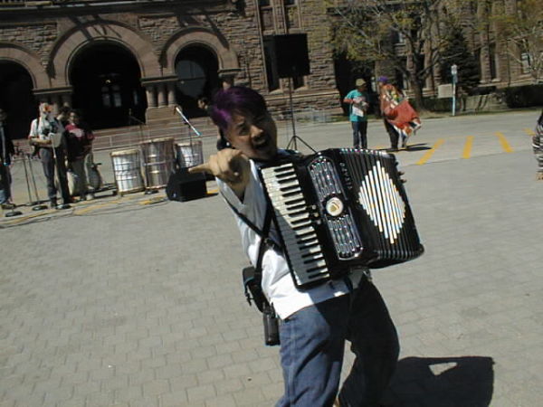 Joey deVilla playing accordion and “throwing the horns” at Queen’s Park