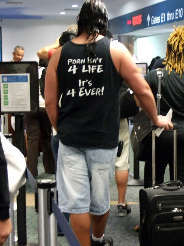 Guy at airport security line wearing tank top that reads \"Porn isn\'t 4 life -- it\'s 4 ever!\"