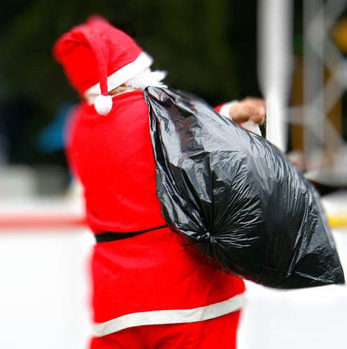 Santa, seen from behind, carrying a large trash bag