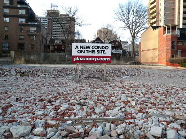 Sign standing in a rubble-covered lot: "A new condo on this site. Plazacorp.com"