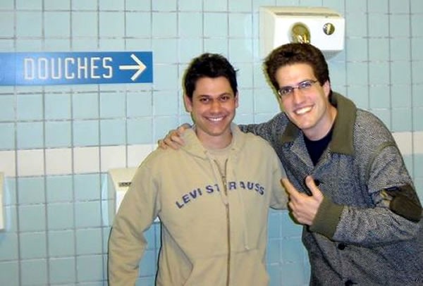 Two guys posing beside a sign in French that points to the showers: "Douches"