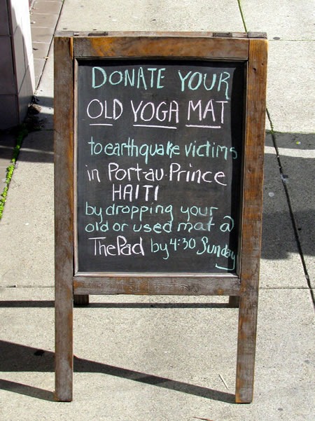 Chalkboard sidewalk sign: "Donate your old yoga mat to earthquake victims in Port-au-Prince, Haiti by dropping your old or used mat @ The Pad by 4:30 Sunday"