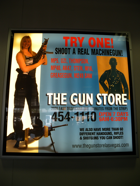 Sign: "Try One! Shoot a real machinegun! MP5, Uzi, Thompson, MP40, AK-47, Sten, M16, Greasegun, M249 SAW. The Gun Store"