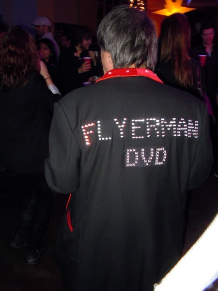 Flyerman, from behind, with his trademark jacket studded with LEDs that spell out "Flyerman DVD"