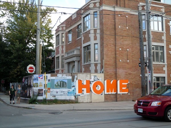 An apartment building under renovation, surrounded by a construction wall with the word "HOME" painted on it in large orange letters