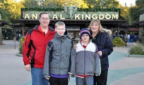 Family posing in front of Disney's "Animal Kingdom" sign, with Dad's head blocking the "im" in "Animal"