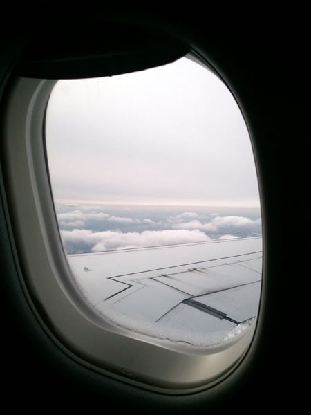 View out of an airplane window, looking at the wing and clouds