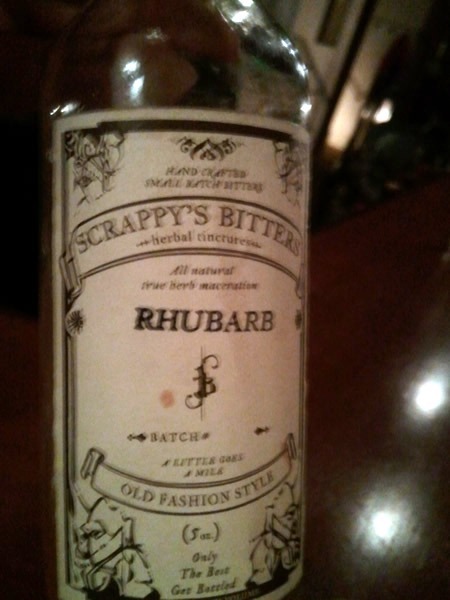 A bottle of bitters. Label reads "Scrappy's Bitters / Herbal Tincture / All natural with herb maceration / RHUBARB / Old Fashion Style"