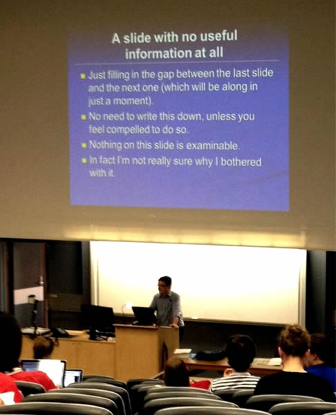 Professor at a university lecture showing a slide: "A slide with no useful information at all / Just filling the gap between the last slide and the next one (which will be along in just a moment) /  No need to write this down (unless you feel compelled to do so) / Nothing on this slide is examinable / In fact, I'm not sure why I bothered with it"