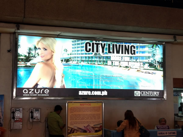 Large billboard ad inside Ninoy Aquino International Airport featuring Paris Hilton promoting a new condo