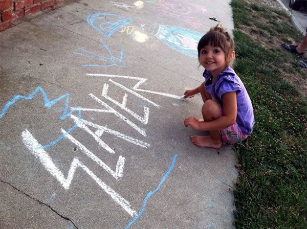 Little girl making a chalk drawing of the Slayer logo on the sidewalk