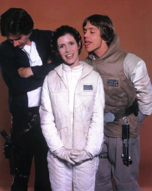 Outtake from a 'Star Wars' promotional photo shoot with Mark Hamill trying to lick Carrie Fisher's ear, as Harrison Ford looks away, embarrassed.