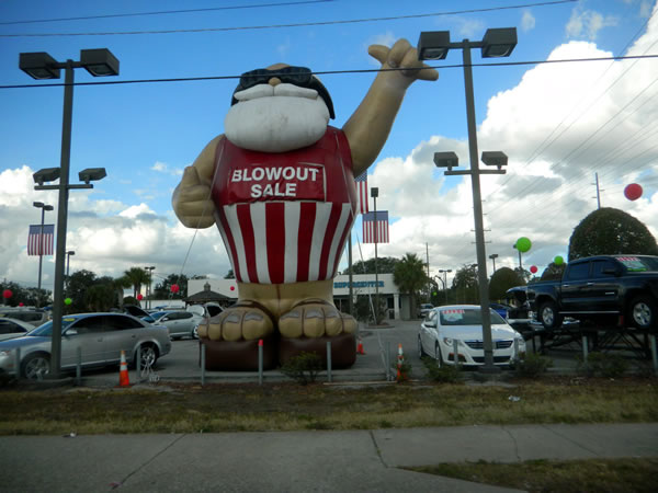 Giant inflatable balloon shaped like an ape with the sign "Blowout sale". The balloon is on an auto dealer's lot.