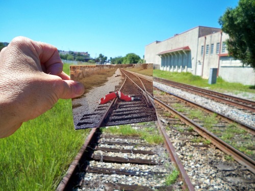 Railroad tracks, with hand holding photo of Santa lying dead across railroad tracks.