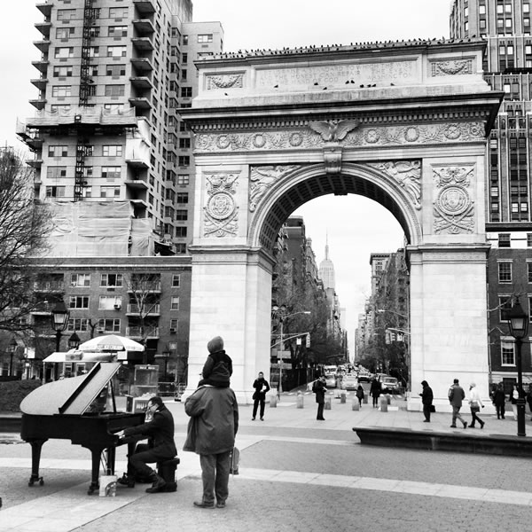 Man playing a grand piano in Washington Square Park as people look on.