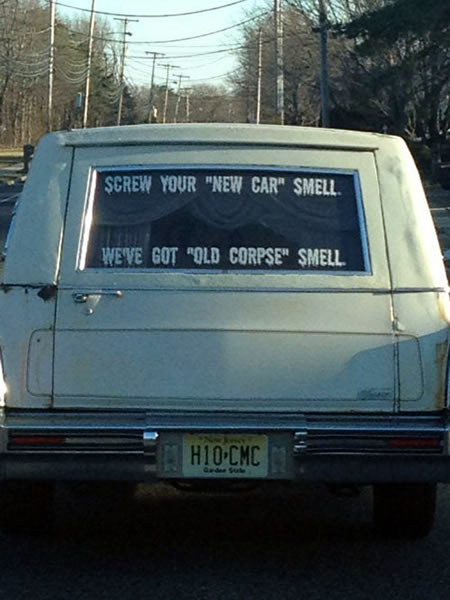 Rear view of hearse with window decal that reads "Screw your new car smell / We've got old corpse smell".