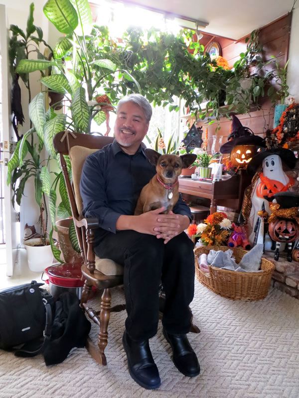 Joey deVilla, sitting in a rocking chair with a chihuahua/dachsund cross in his lap, in a room full of Hallowe'en decorations.