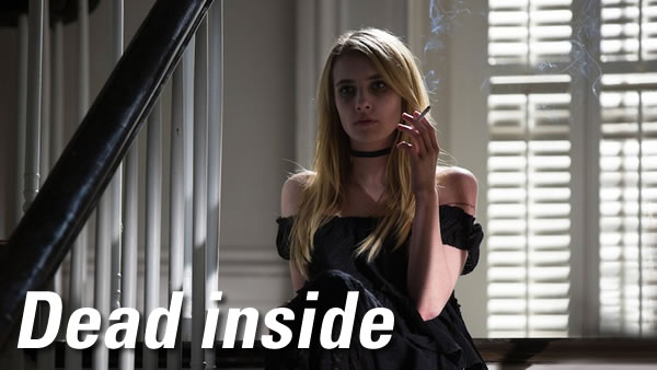Dead inside: A young blonde woman in a black dress with bare shoulders, sitting at the top of a staircase and smoking a cigarette with a vacant expression on her face.