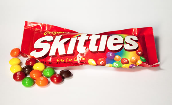 Bag of Skittles with some inidividual Skittles candies beside it.