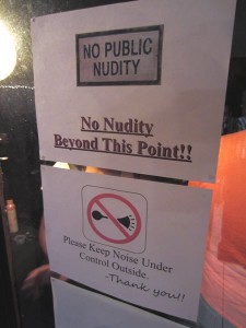 Laser-printed sign taped onto a sliding glass door leading outside: "NO PUBLIC NUDITY. No nudity beyond this point!"