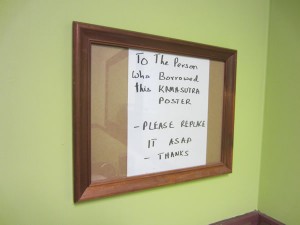 Sign inside frame: "To the person who borrowed the KAMASUTRA poster: please replace it ASAP -- THANKS"