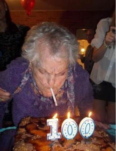Old person lighting a cigarette with one of the "100" candles on his/her birthday cake