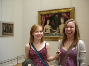 Two young women at The Louvre reenacting the Gabrielle d'Estrées et une de ses soeurs painting (the one where one nude woman pinches the nipple of the nude woman beside her), which is behind them
