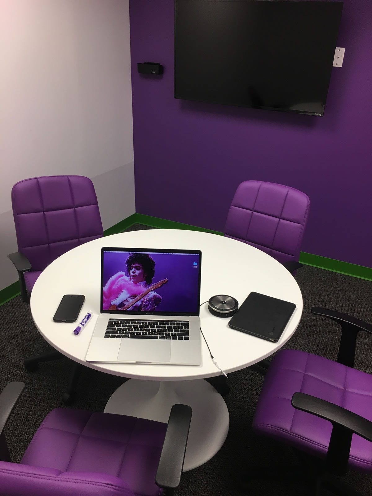 Photo: Sourcetoad's 'Purple Passion Pit' - a small room with a white table, 4 purple chairs, and a purple wall with a monitor. On the table are a purple dry-erase marker and a Macbook Pro with an image of Prince on its monitor.