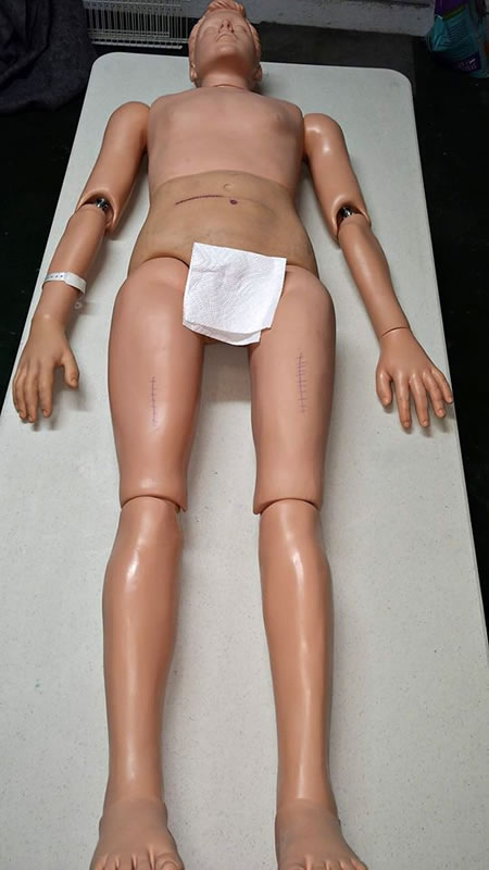 Full photo of medical mannequin laid out on a table, with towel covering its genital area