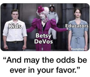 Photo: Scene from “The Hunger Games” where host Effie Trinket (labeled “Betsy DeVos” stands between new tributes Peta Mellark (labeled “Kids”) and Katniss Everdeen (labeled “Educators”). The caption reads “And may the odds be ever in your favor.”