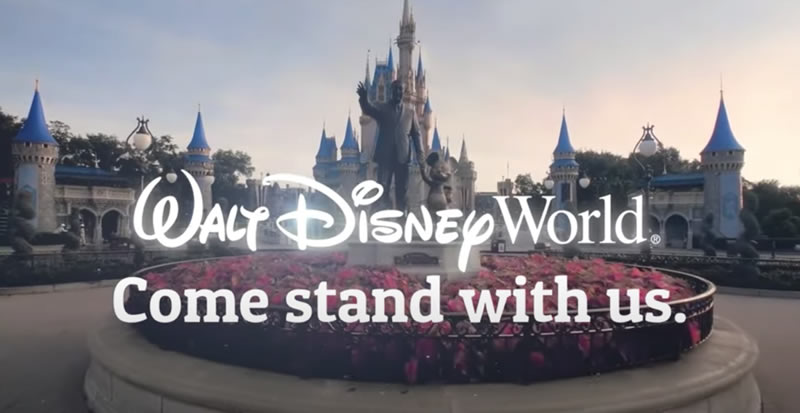 Photo: The entrance to the Magic Kingdom park, with the Walt Disney and Mickey statue in the foreground, overlaid with the text: “Walt Disney World / Come stand with us”.