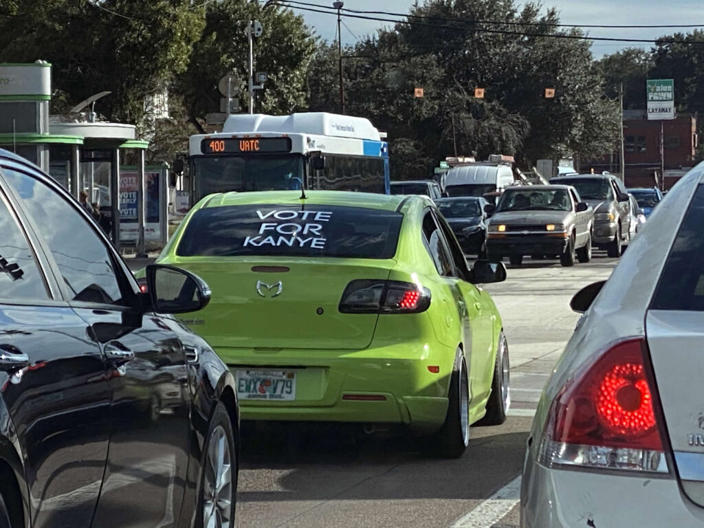 Photo: Lime green Mazda hatchback with a big “VOTE FOR KANYE” sticker on its rear windshield.