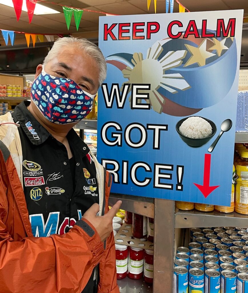Joey deVilla, at Tampa’s Philippine Grocery, posing beside a sign that read “KEEP CALM: WE GOT RICE!”.