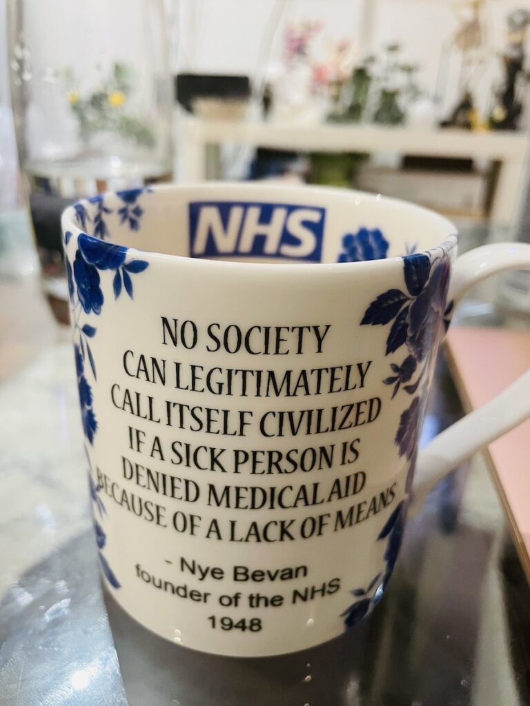NHS mug, with the NHS logo on its inside and this written on the outside: “No society can legitimately call itself civilized if a sick person is denied medical aid because of a lack of means. — Nye Bevan, founder of the NHS, 1948””