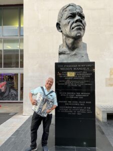 Joey deVilla poses with his accordion beside a bust of Nelson Mandela near National Theatre, London, UK.