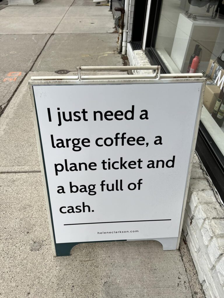 “Sandwich board” sign outside a coffee shop that reads “I just need a large coffee, a plane ticket, and a bag full of cash.”