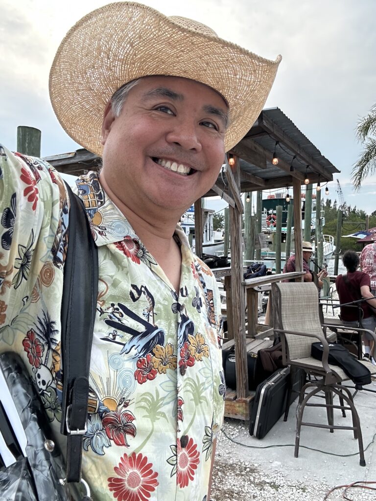 Joey deVilla in a cowboy hat and aloha short. In the background is a fishing shed and the dock behind Bayou Bistro.