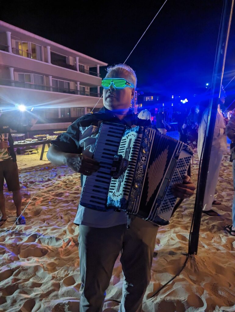 Joey deVilla on a beach at night, playing the accordion while wearing electrolumninescent wire sunglasses.