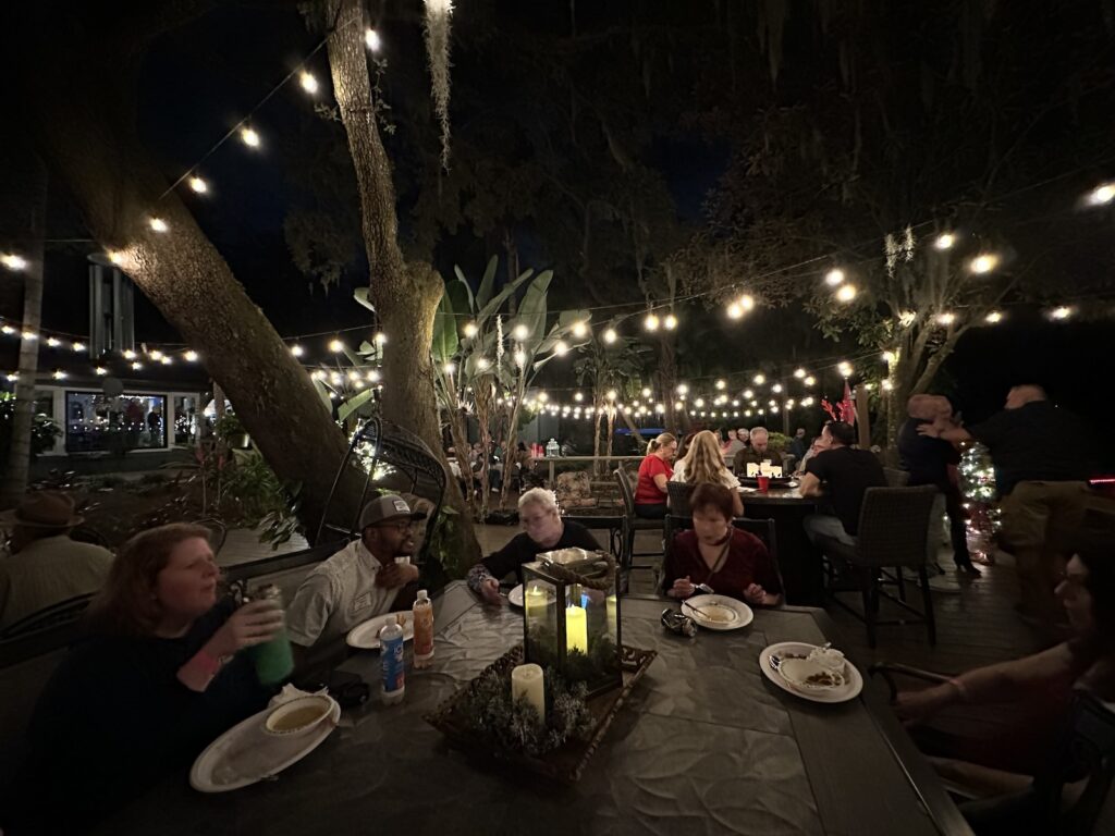 People dining in a large backyard with string lights overhead.