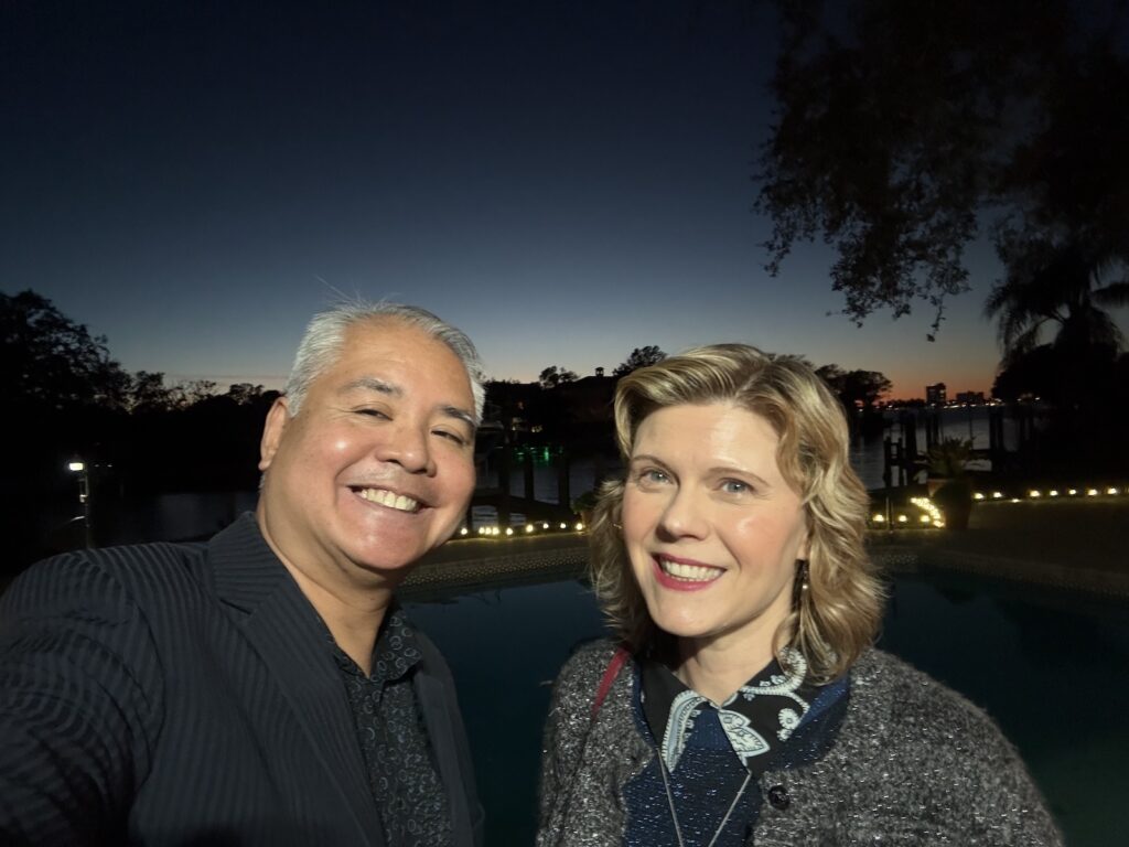 Joey de Villa and Anitra Pavka, in front of a dock on Davis Islands at twilight, with Tampa Bay in the background. 